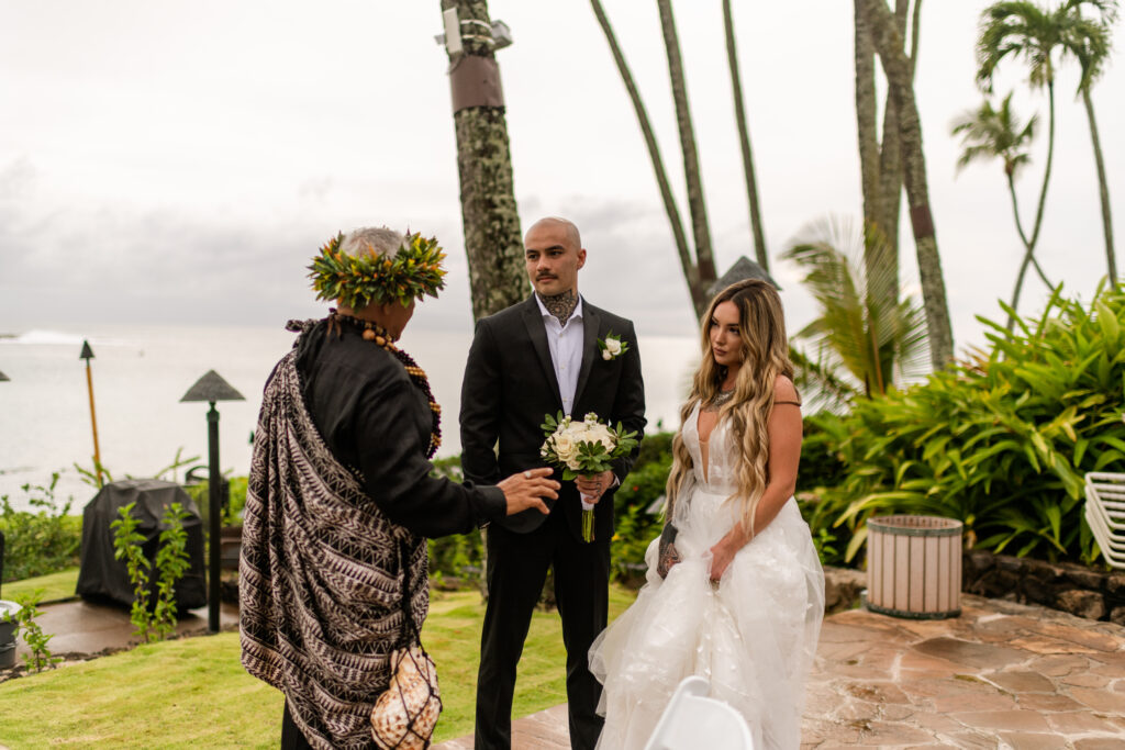 Couple stands with officiant overlooking sea at small Maui beach wedding.