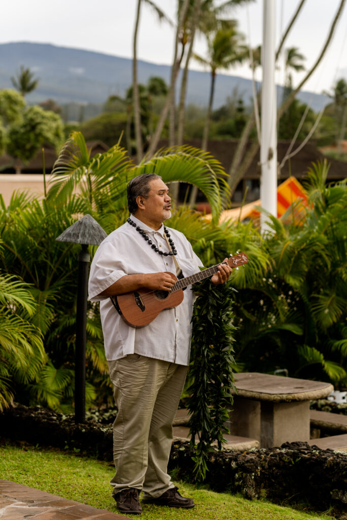 Ukulele musician in white shirt and lei plays during Maui beach wedding ceremony.