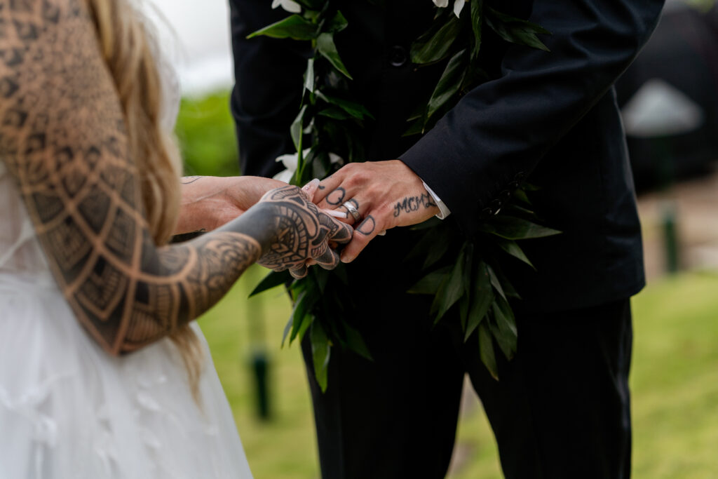 Close up of bride placing the ring on her groom’s finger in Maui