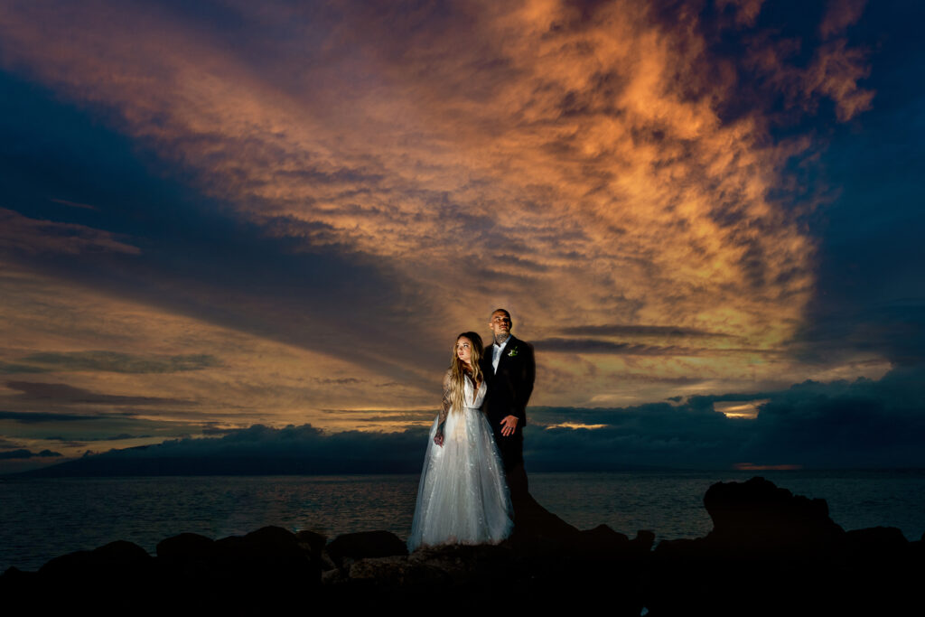 Bride and groom standing on stones with sunset rays behind them after their Maui wedding