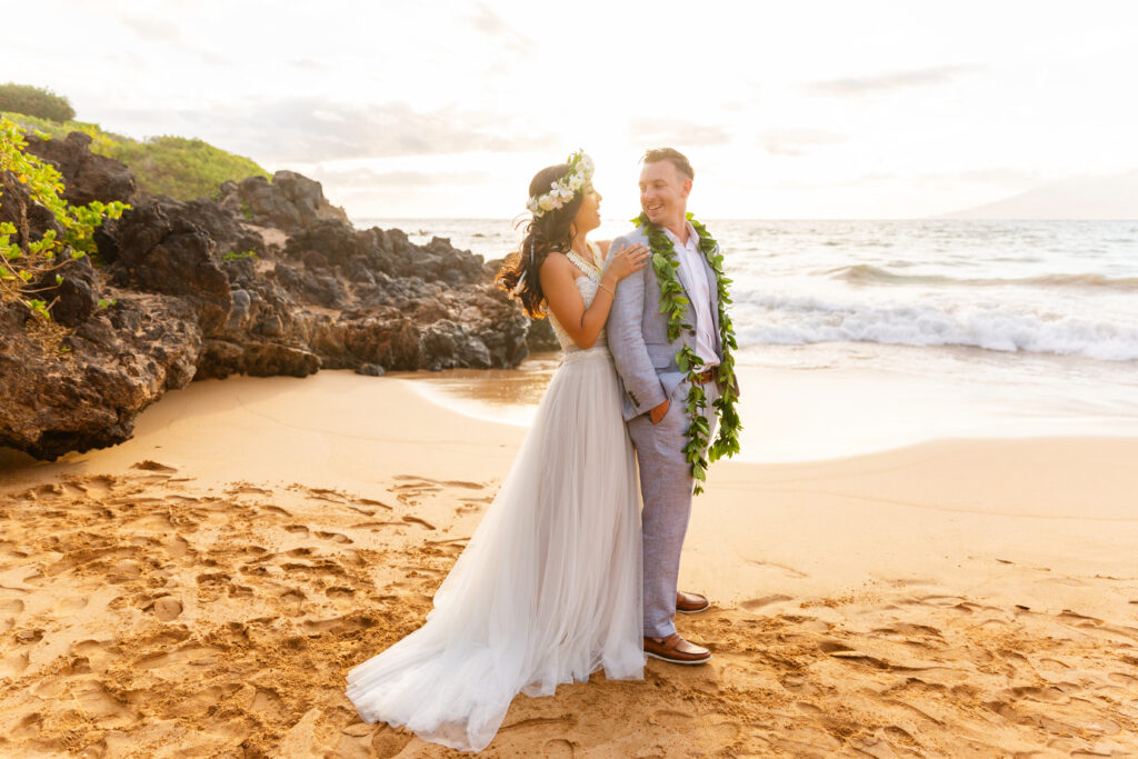 Couple embracing with ocean waves behind them at a Maui elopement