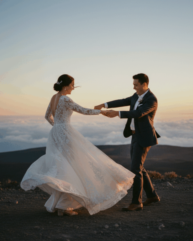 Romantic Haleakala sunset wedding on Maui: elegant bride in lace long-sleeve gown twirling with groom in suit atop volcano crater, dress billowing against orange skies and misty clouds, perfect 2026 elopement inspiration.