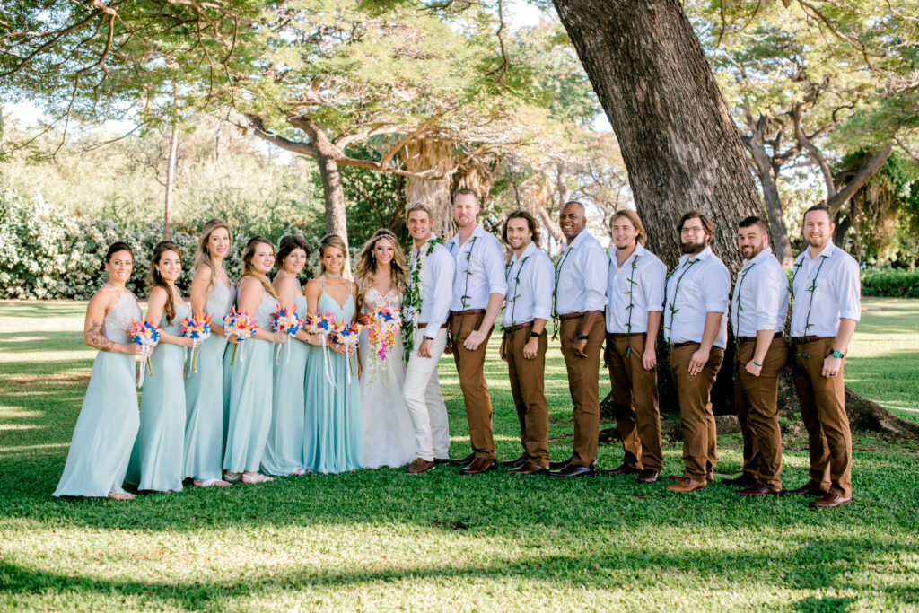 Wedding party standing in a garden, bridesmaids in light blue dresses and groomsmen in white shirts and tan pants beside the bride and groom.