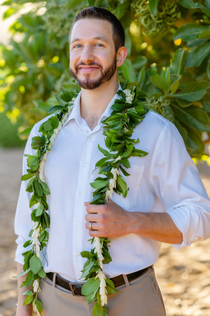 Groom in an ivory linen suit and Panama hat wearing a white lei at an oceanfront Maui venue.