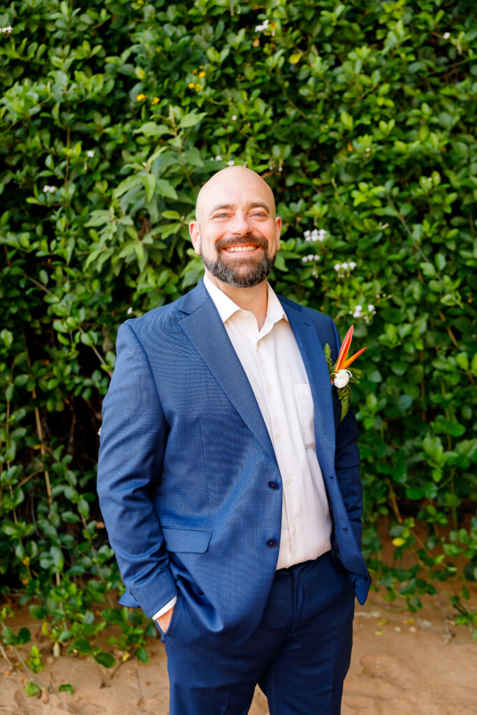 Groom in a bright blue suit and white shirt with a green maile style lei on a Maui shoreline.