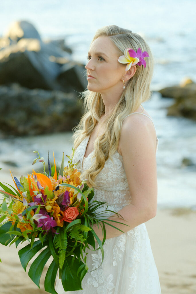 Bride in an elegant off shoulder wedding dress standing on the sand at her Maui ceremony site.

