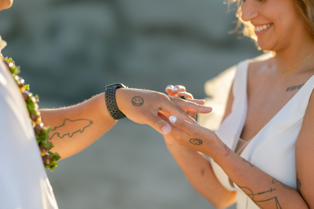 Couple exchanging rings at Ironwood Beach Kapalua with matching smiley tattoos on their fingers