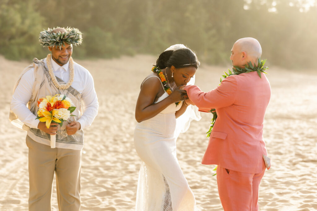 Bride kissing groom’s hand during their Maui beach elopement ceremony while the officiant looks on