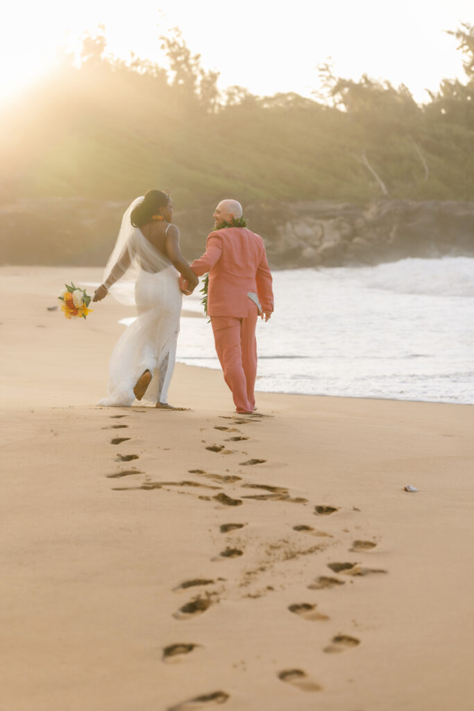 Bride and groom walking away together leaving footprints in the sand at their Maui beach elopement