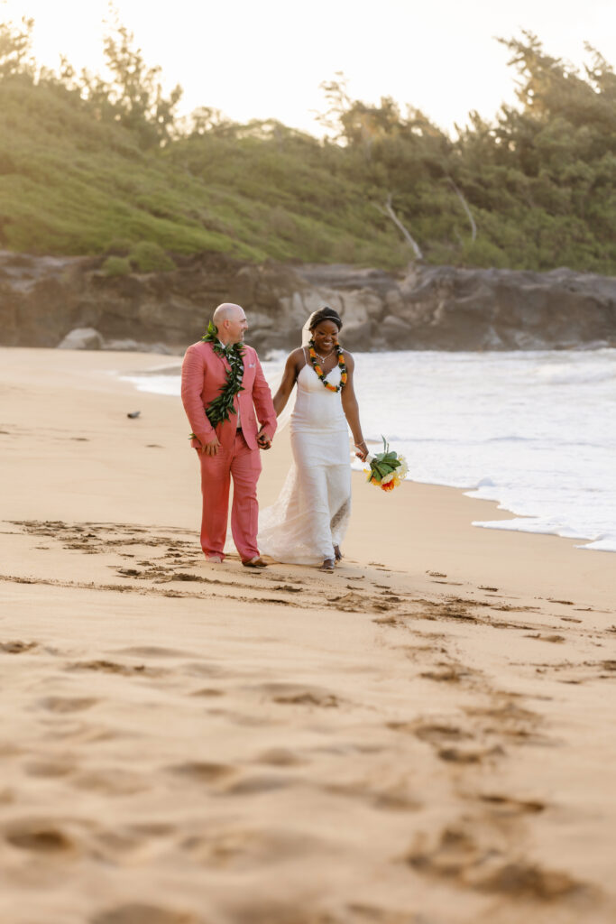 Newlyweds walking barefoot along the shoreline at sunset during their Maui beach elopement