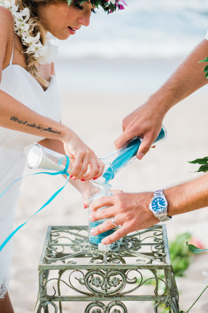 Bride and groom pouring colored sand into a keepsake bottle during a Maui beach wedding ceremony.