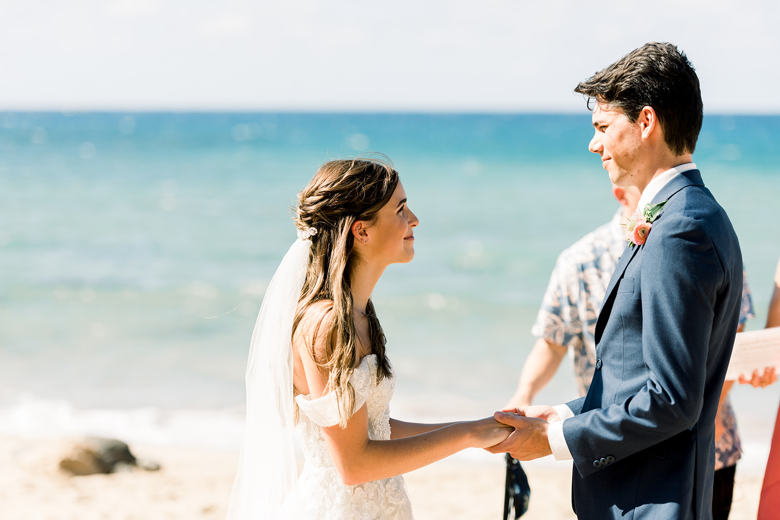 Bride and groom holding hands during their Maui beach wedding ceremony with ocean views behind them.