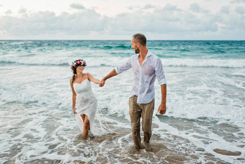 Newlywed couple walking hand in hand through the surf after their Maui beach wedding ceremony.