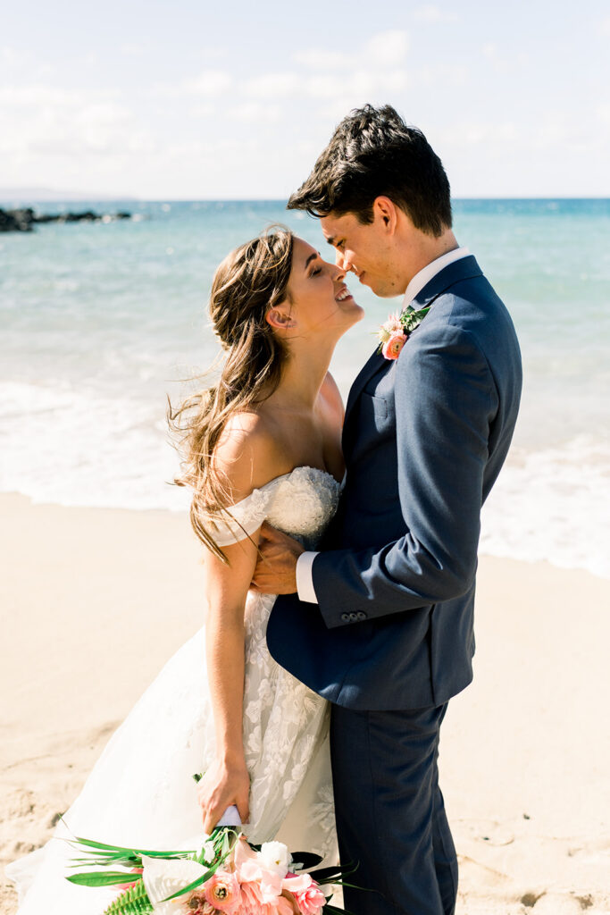 Newly married couple embracing on a Maui beach after their destination wedding ceremony.