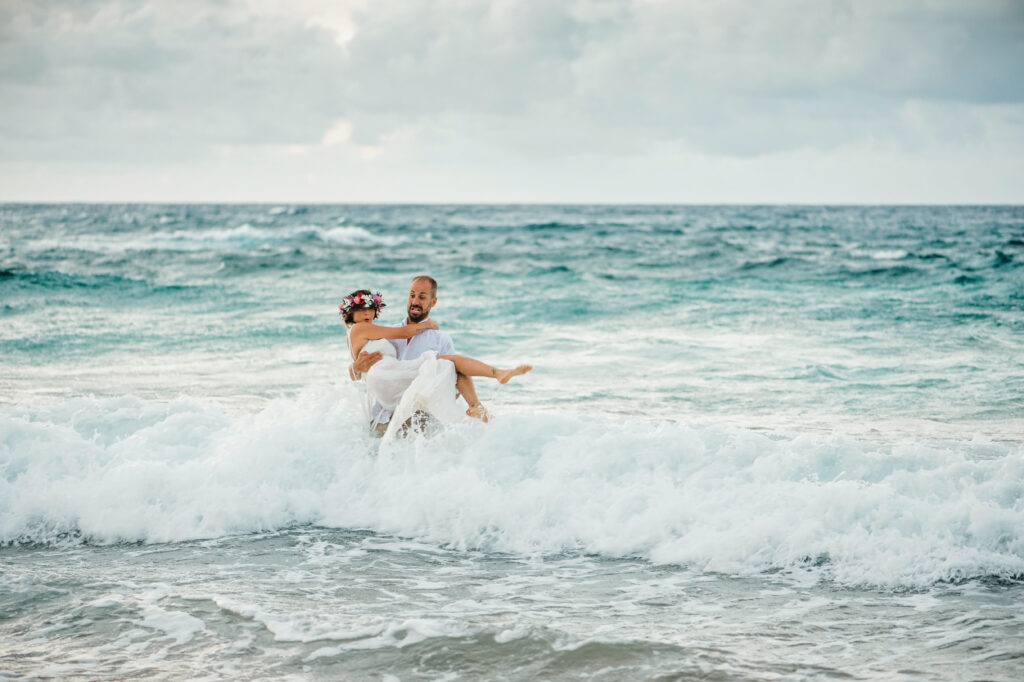 Bride and groom embracing in the ocean waves during a playful Maui beach wedding portrait session.