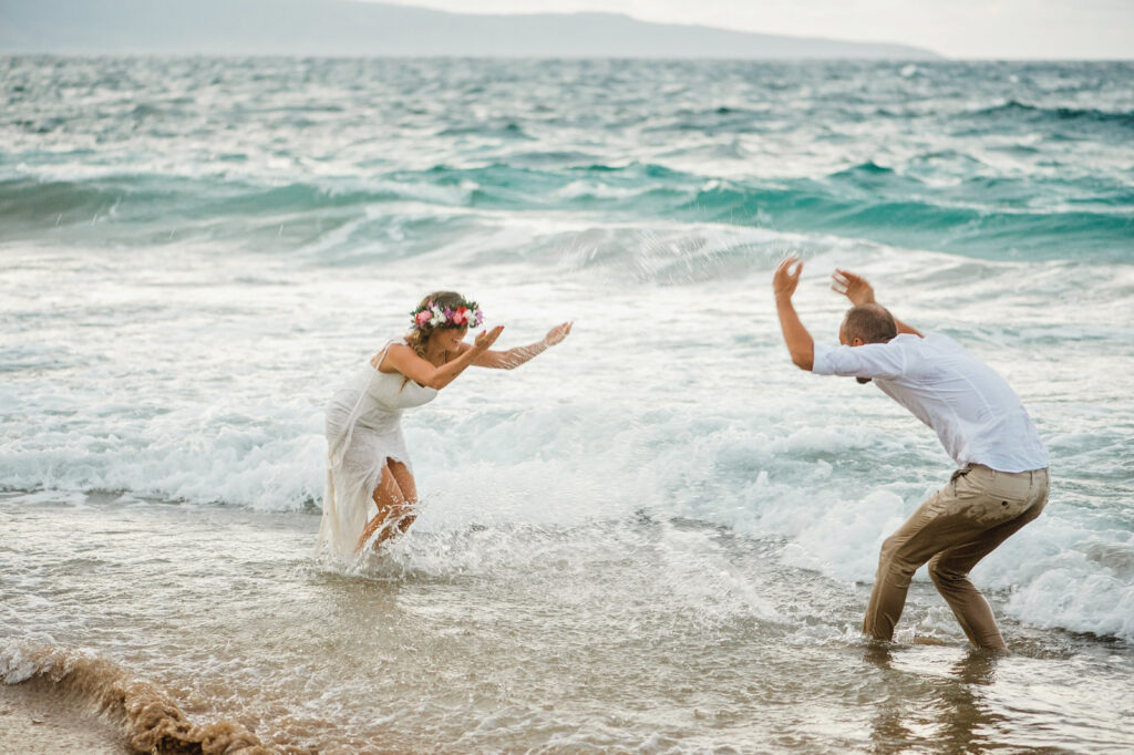 Bride and groom laughing and splashing water at each other in the surf during their Maui elopement celebration.
