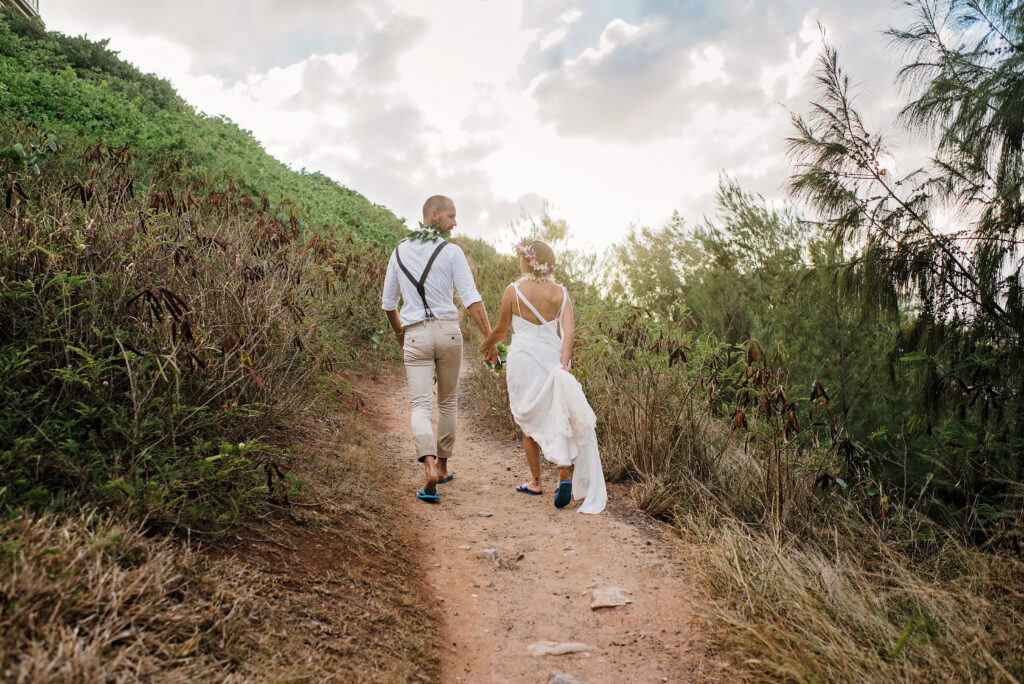 Newlywed couple walking hand in hand along a coastal trail after their Maui beach wedding.