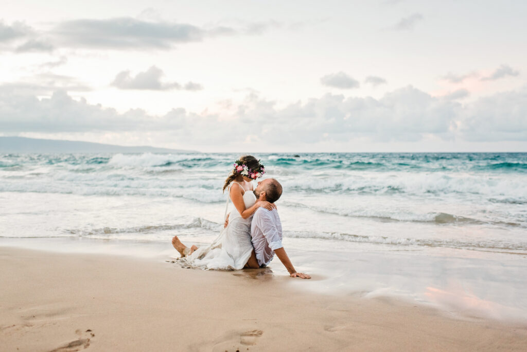 Bride sitting on her groom's lap on the shoreline during a romantic Maui beach wedding portrait session.
