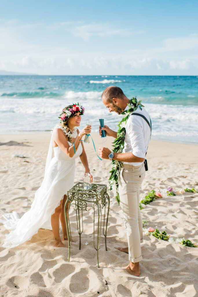 Couple smiling during a sand ceremony at their Maui beach wedding with ocean waves in the background.