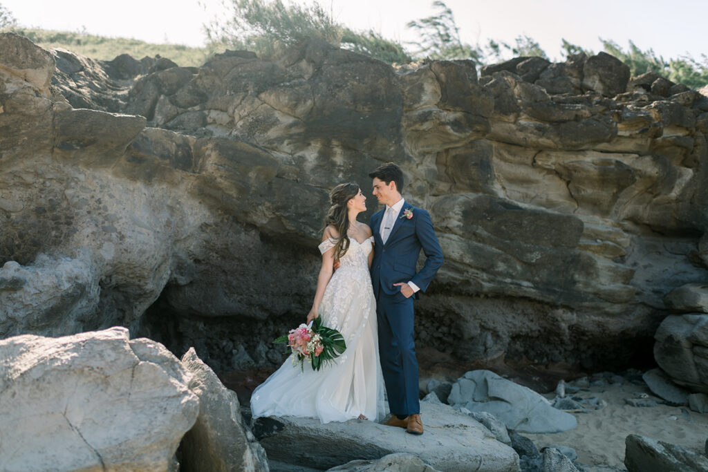Bride holding a tropical bouquet while standing with her groom along Maui's coastline.